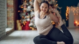 An image of a happy woman in a yoga pose, sitting on the floor of her living room