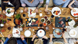 A long table featuring many healthy dishes and the hands of diners who are about to eat the food