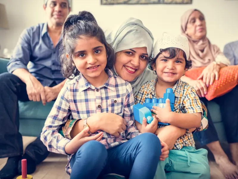 A Muslim family sitting on and around the sofa in their living room loading=