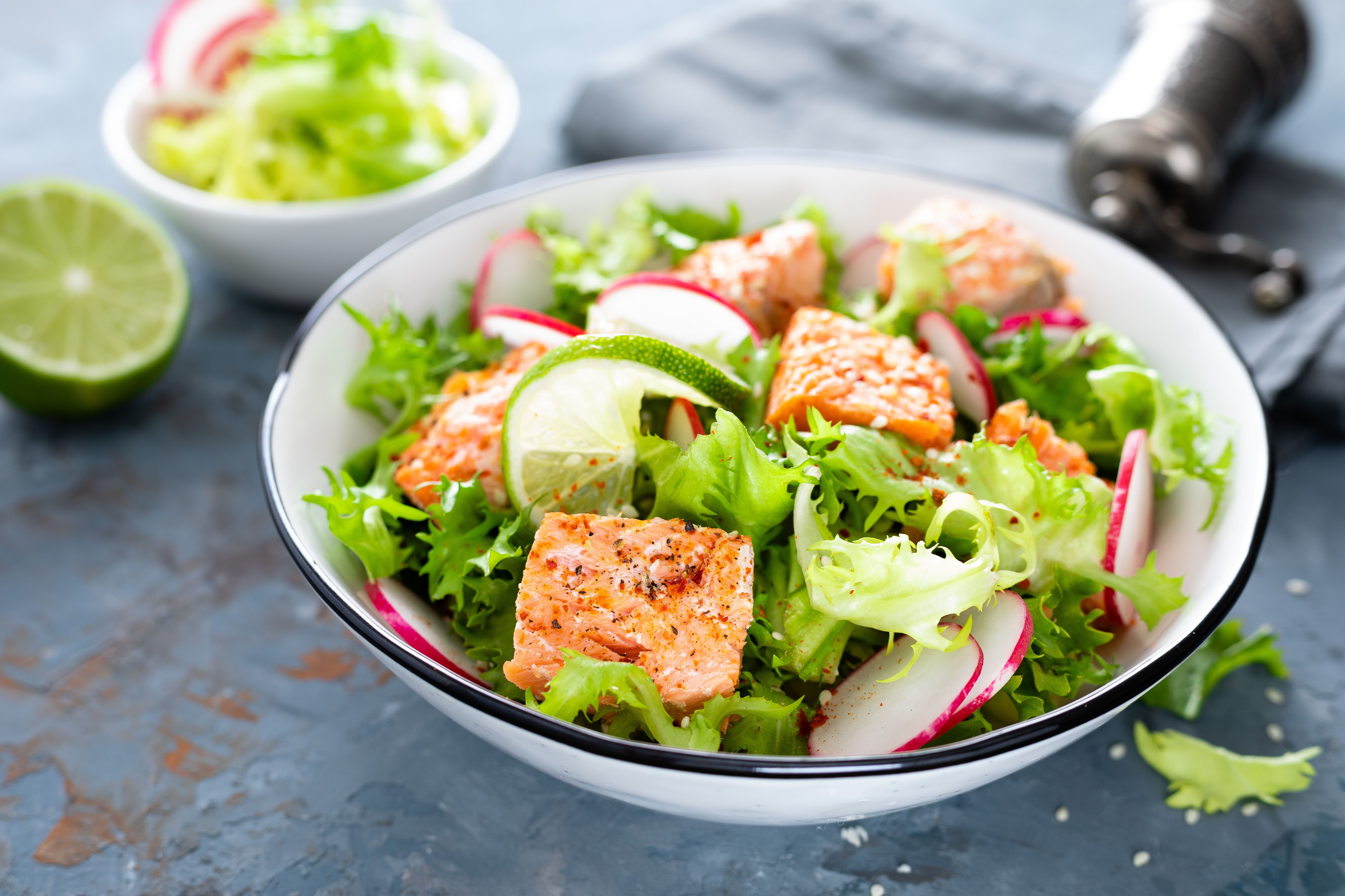 A fresh salad in a bowl, containing salmon, lettuce, courgette, radish and lime.