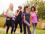 A diverse group of happy ladies, carrying yoga mats through a garden