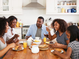 A happy family eating breakfast together in their kitchen, around a wooden table