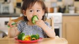 A young child eating broccoli with her hands