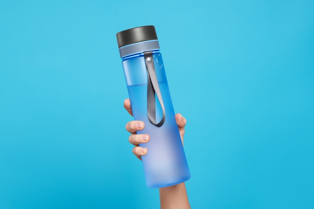 A woman's hand holding a reusable water bottle on a blue background.