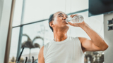 An older asian man in the gym, drinking water to rehydrate