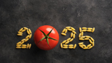 A chalkboard background with the word '2025' written on it. The letters are formed from pasta, except the zero, which is replaced by a tomato