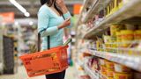 An image of a lady in a supermarket holding a basket and deciding on what to buy